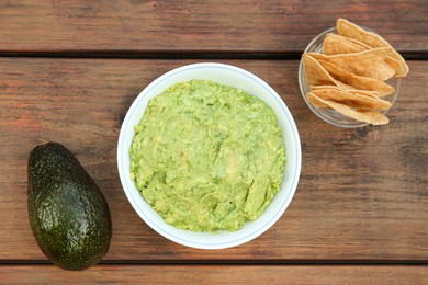 Delicious guacamole, avocado and nachos on wooden table, flat lay