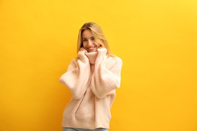 Beautiful young woman wearing knitted sweater on yellow background