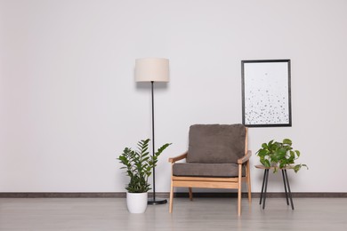 Stylish armchair, floor lamp and plants near white wall, space for text. Interior design