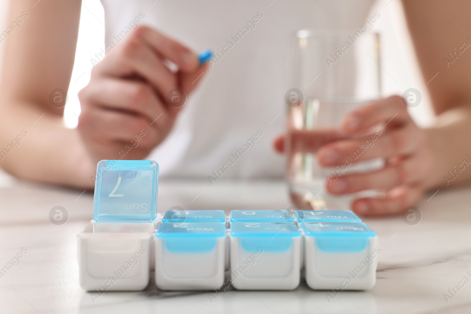 Photo of Woman with pills, organizer and glass of water at white marble table, selective focus