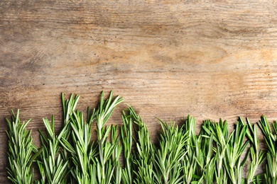 Photo of Branches of fresh rosemary on wooden table, top view with space for text