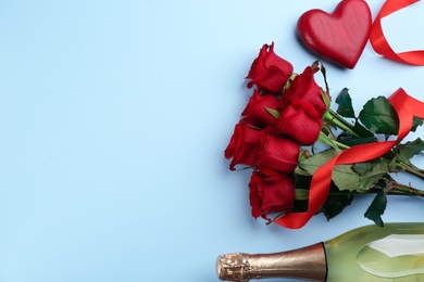 Flat lay composition with beautiful red roses and bottle of champagne on light blue background, space for text. Valentine's Day celebration