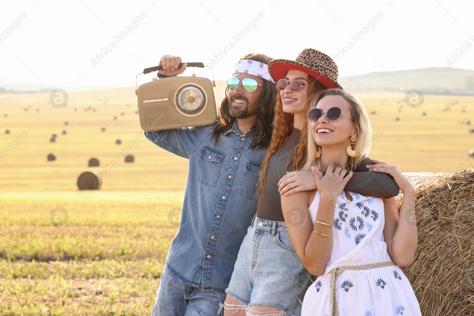 Photo of Happy hippie friends with radio receiver near hay bale in field, space for text