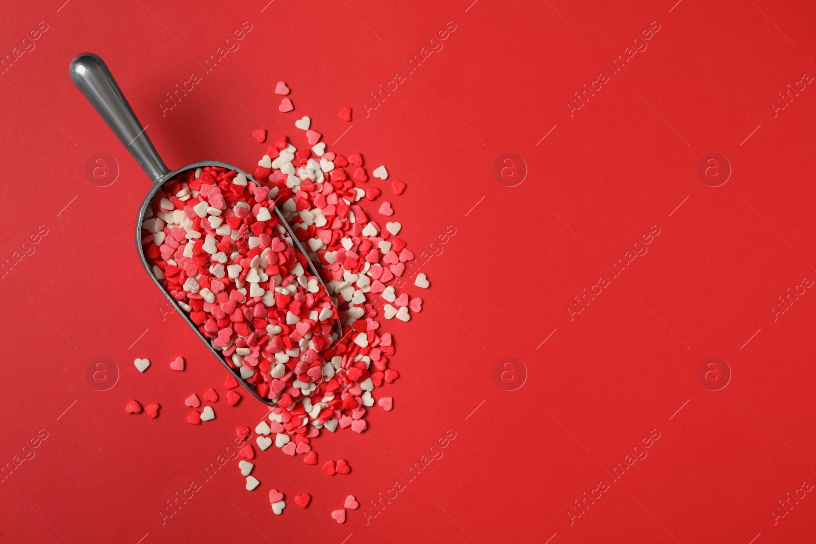 Photo of Bright heart shaped sprinkles in scoop on red background, flat lay. Space for text