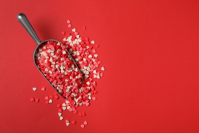 Bright heart shaped sprinkles in scoop on red background, flat lay. Space for text