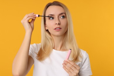 Photo of Beautiful woman applying mascara on orange background