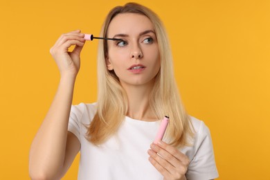 Beautiful woman applying mascara on orange background