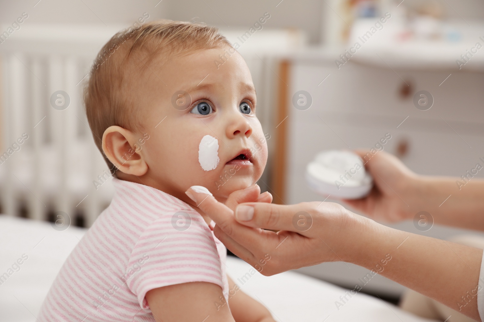 Photo of Mother applying moisturizing cream on her little baby at home, closeup