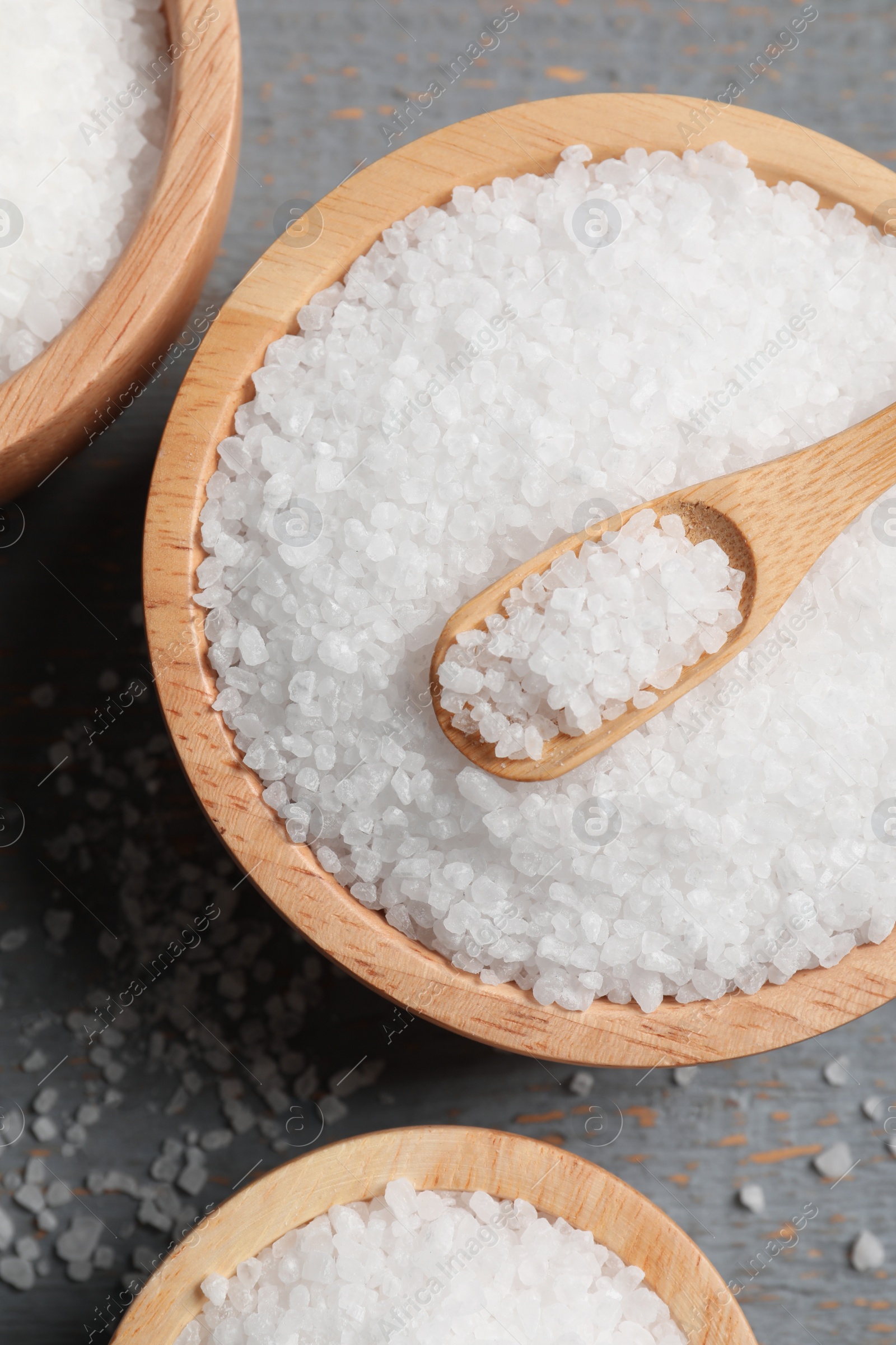 Photo of Bowls of natural sea salt on grey wooden table, flat lay