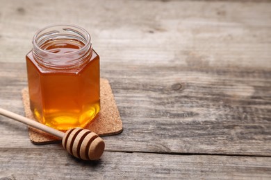 Photo of Sweet honey in jar and dipper on wooden table, space for text