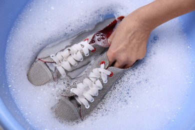 Photo of Woman washing sport shoes in plastic basin, top view