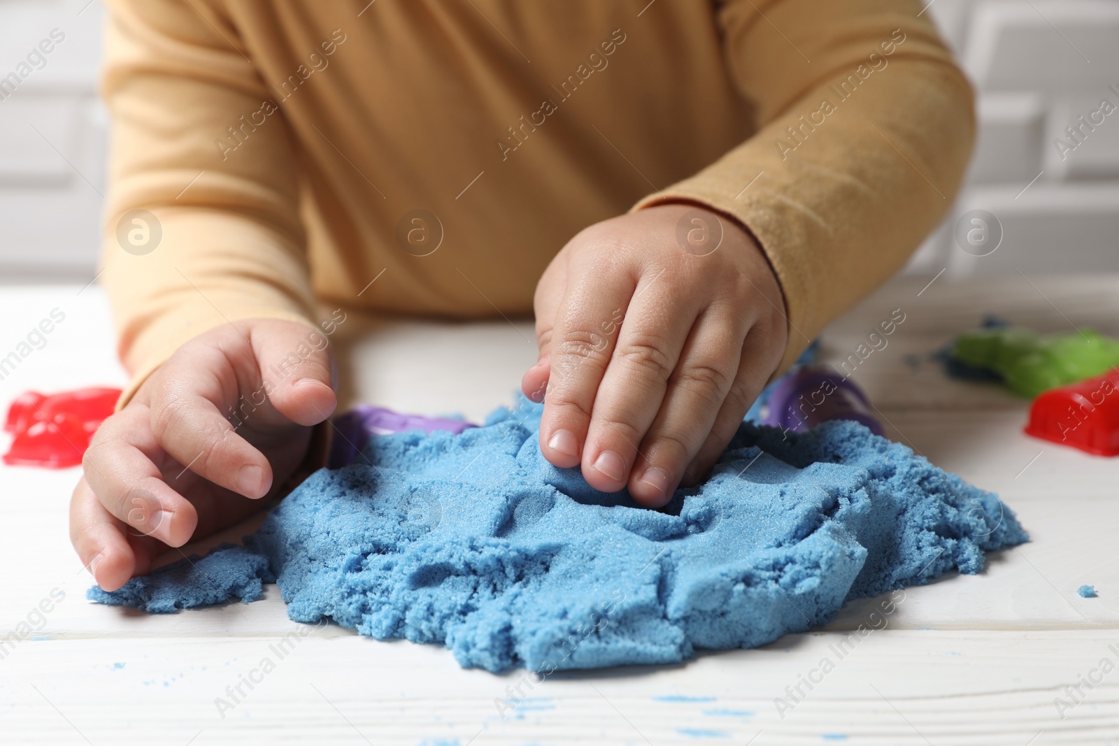 Photo of Little child playing with light blue kinetic sand at white wooden table, closeup