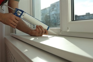 Man sealing window with caulk indoors, closeup