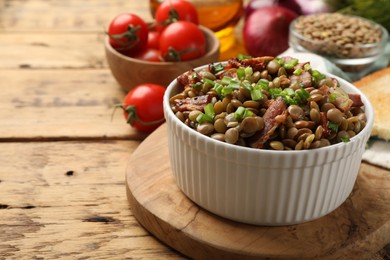 Delicious lentils with bacon and green onion in bowl served on wooden table, closeup. Space for text