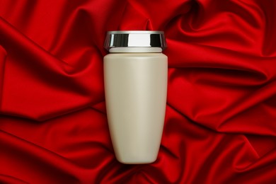Bottle of hair care cosmetic product on red fabric, top view