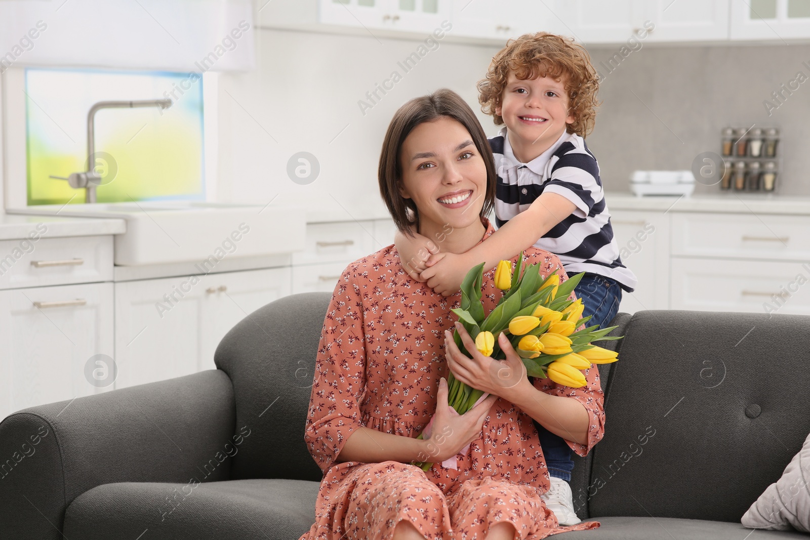 Photo of Little son congratulating his mom with Mother`s day at home, space for text. Woman holding bouquet of yellow tulips