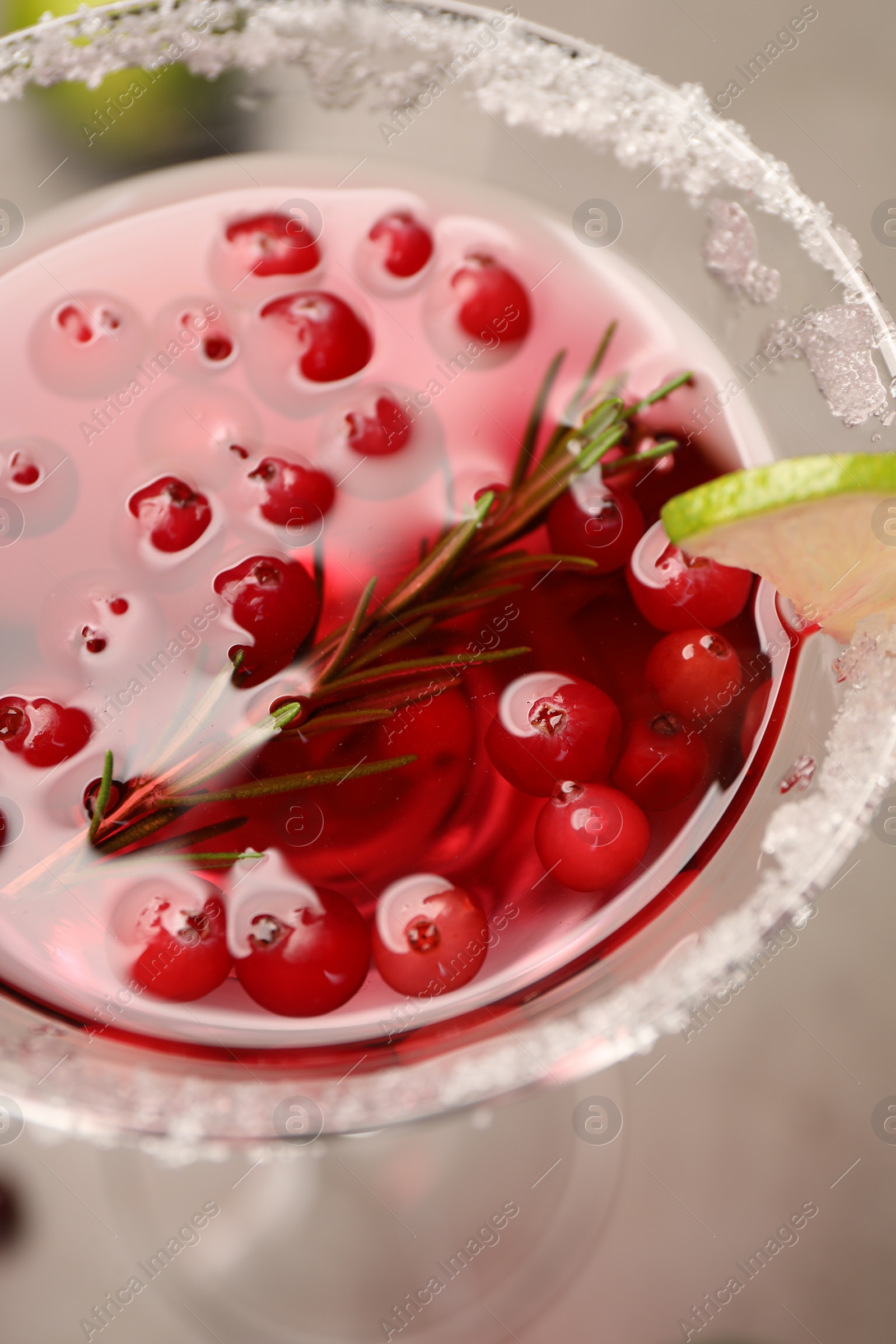 Photo of Tasty cranberry cocktail with rosemary and lime in glass on grey table, closeup