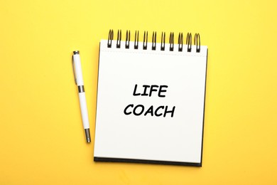 Image of Phrase Life Coach written in notebook and pen on yellow background, top view