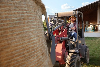 Photo of Smiling farmer in loader transporting hay on farm