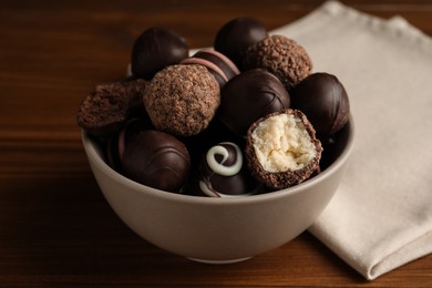 Photo of Many different delicious chocolate truffles in bowl on wooden table