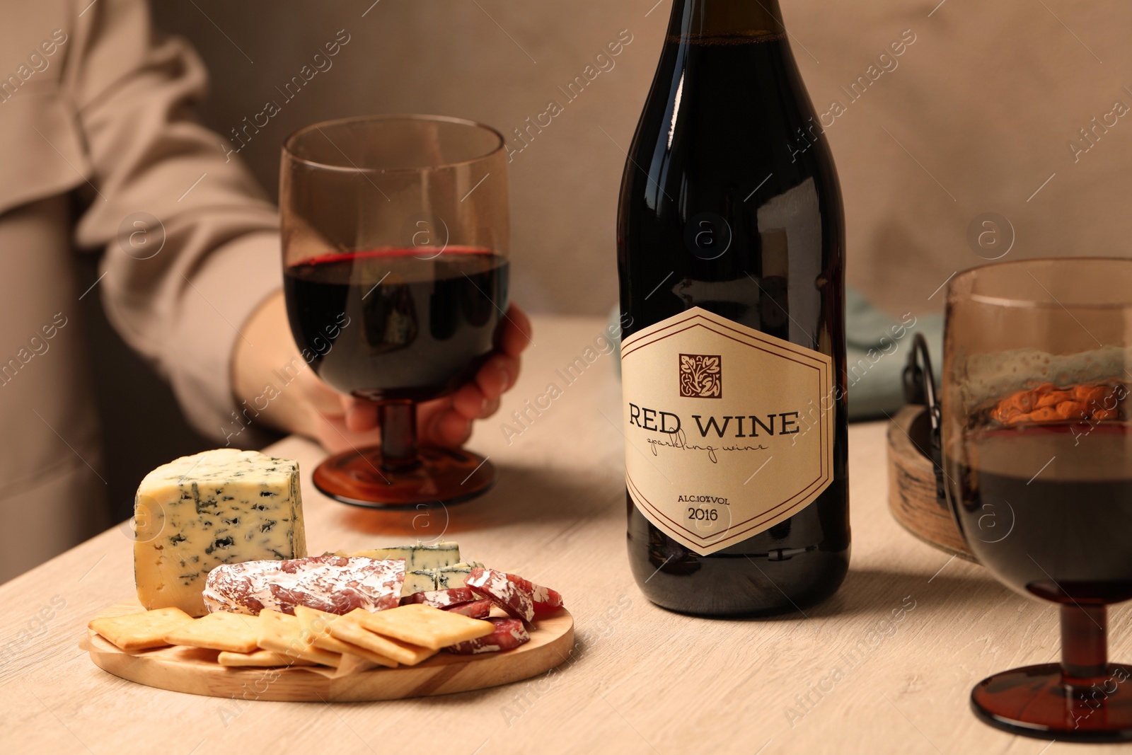 Photo of Woman holding glass of red wine at table with different snacks, closeup