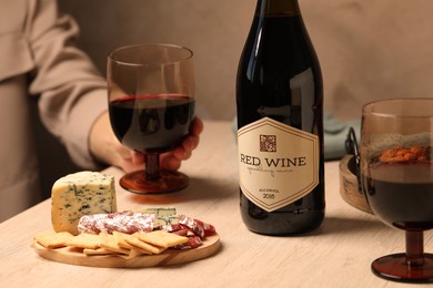 Photo of Woman holding glass of red wine at table with different snacks, closeup