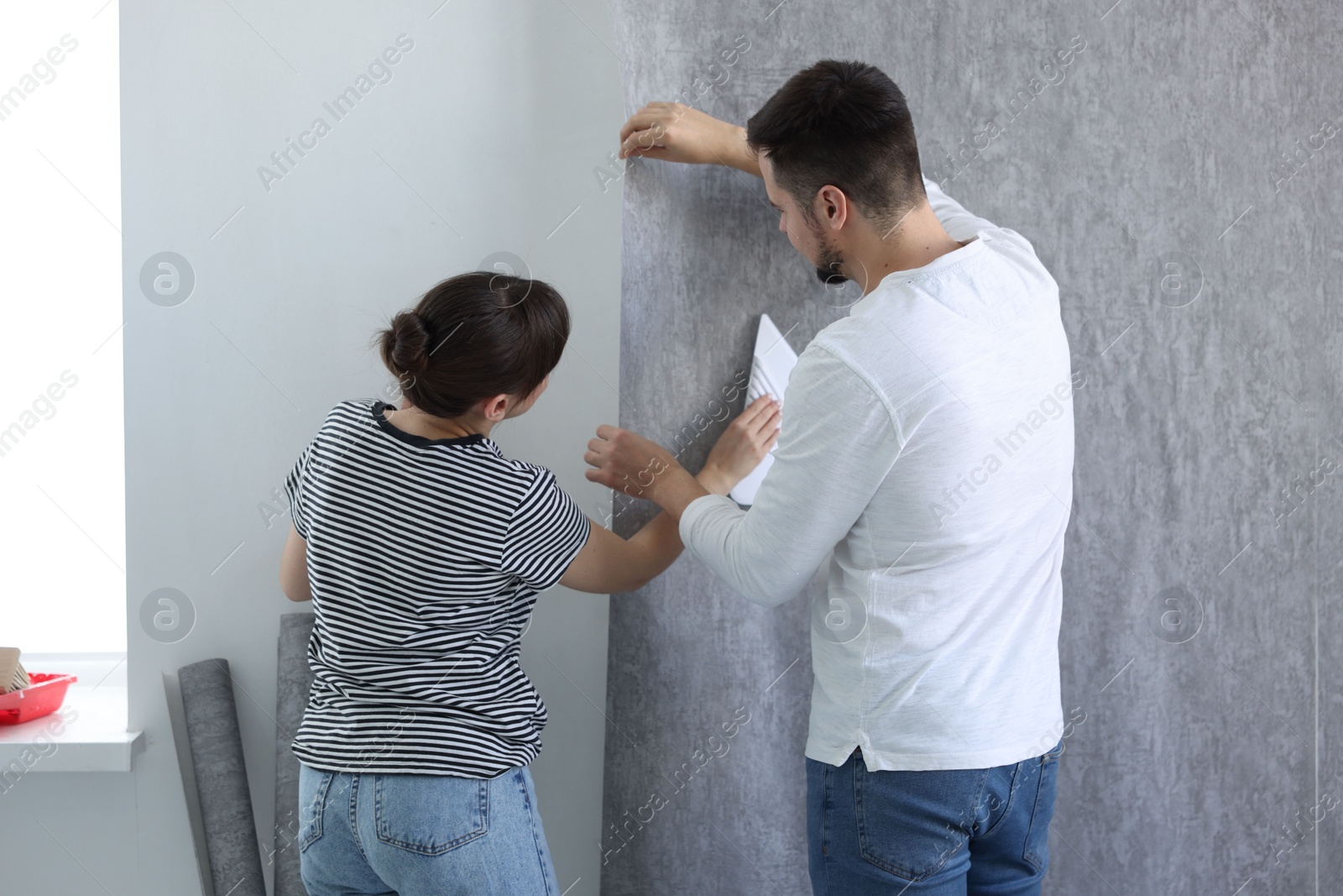 Photo of Woman and man hanging gray wallpaper in room, back view