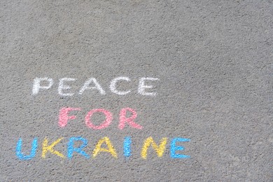 Photo of Words Peace For Ukraine written with colorful chalks on asphalt outdoors, space for text