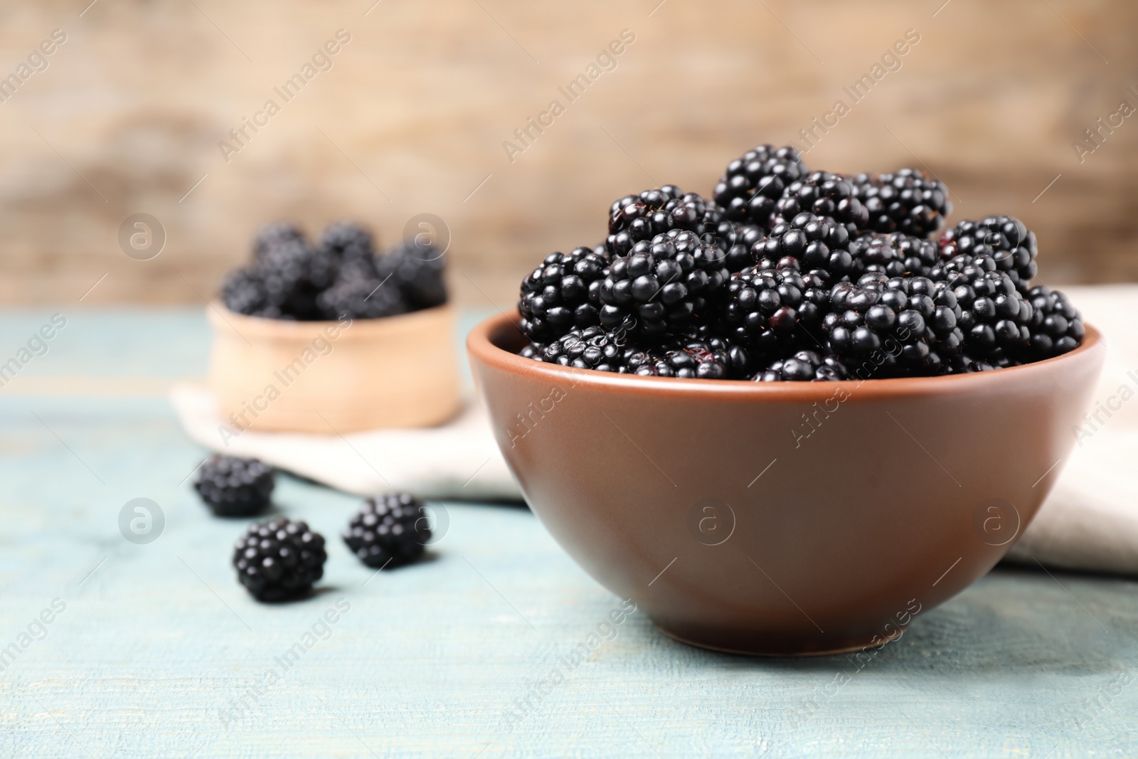 Photo of Fresh ripe blackberries in bowl on blue wooden table. Space for text