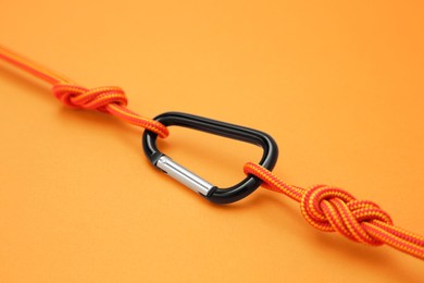 Photo of One metal carabiner with ropes on orange background, closeup