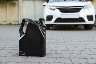 Canister with motor oil near car outdoors, space for text