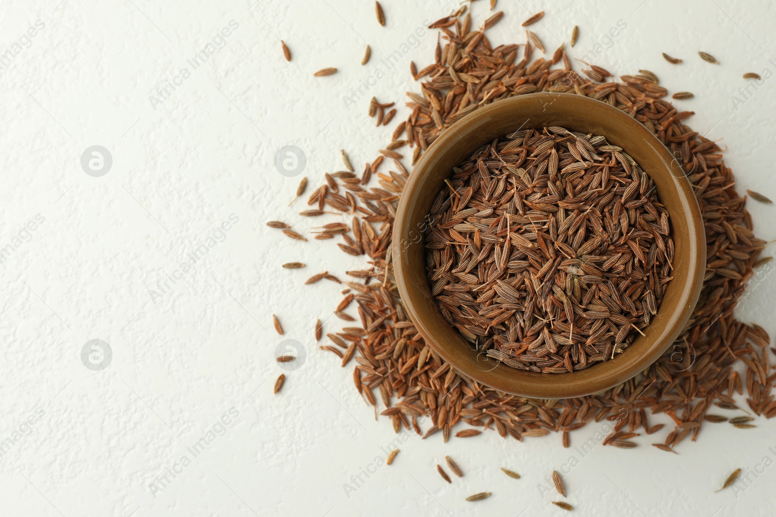 Photo of Caraway (Persian cumin) seeds and bowl on white table, top view. Space for text