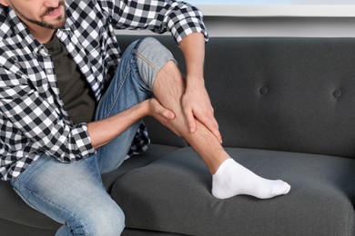 Photo of Man rubbing sore leg on sofa at home