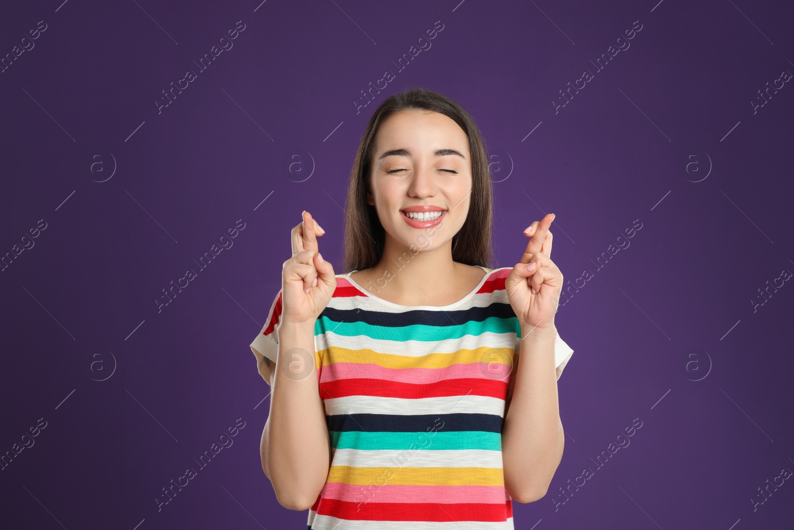 Photo of Woman with crossed fingers on purple background. Superstition concept