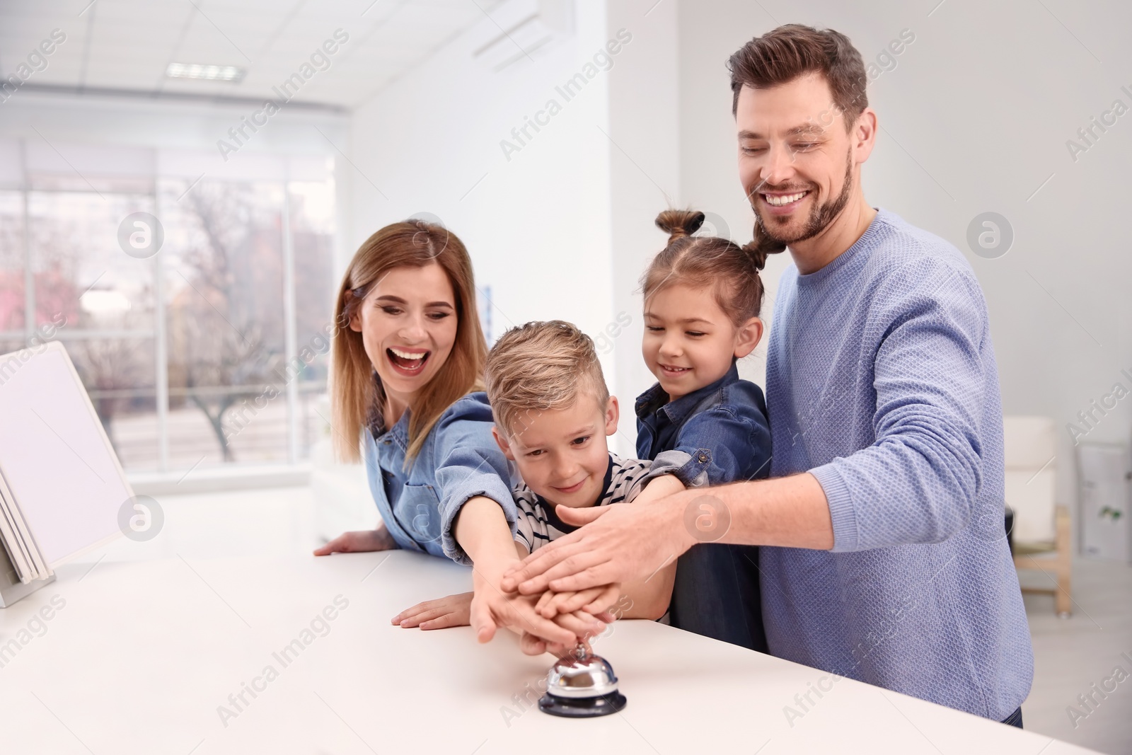 Photo of Family ringing service bell on reception desk in hotel