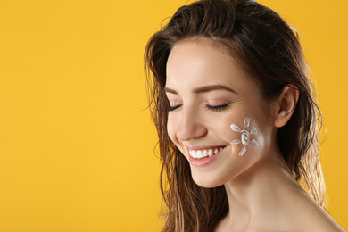 Young woman with sun protection cream on face against yellow background. Space for text