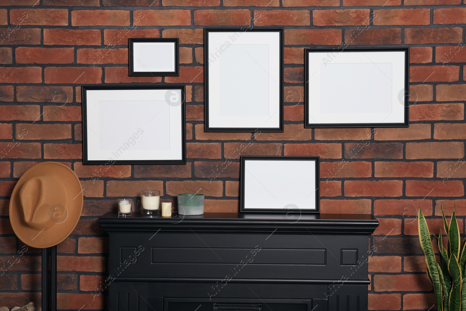 Photo of Empty frames, hat and scented candles on fireplace indoors