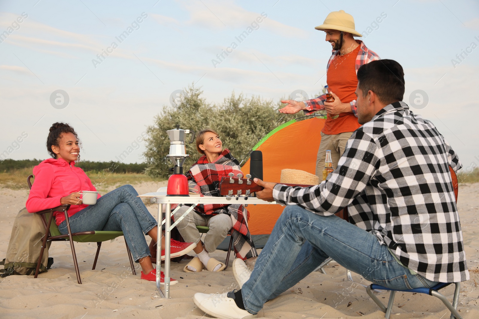 Photo of Friends resting near camping tent on sandy beach