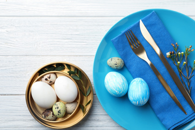 Festive Easter table setting with eggs and floral decoration on wooden background, flat lay