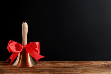 Photo of Golden bell with red bow on wooden table near blackboard, space for text. School days