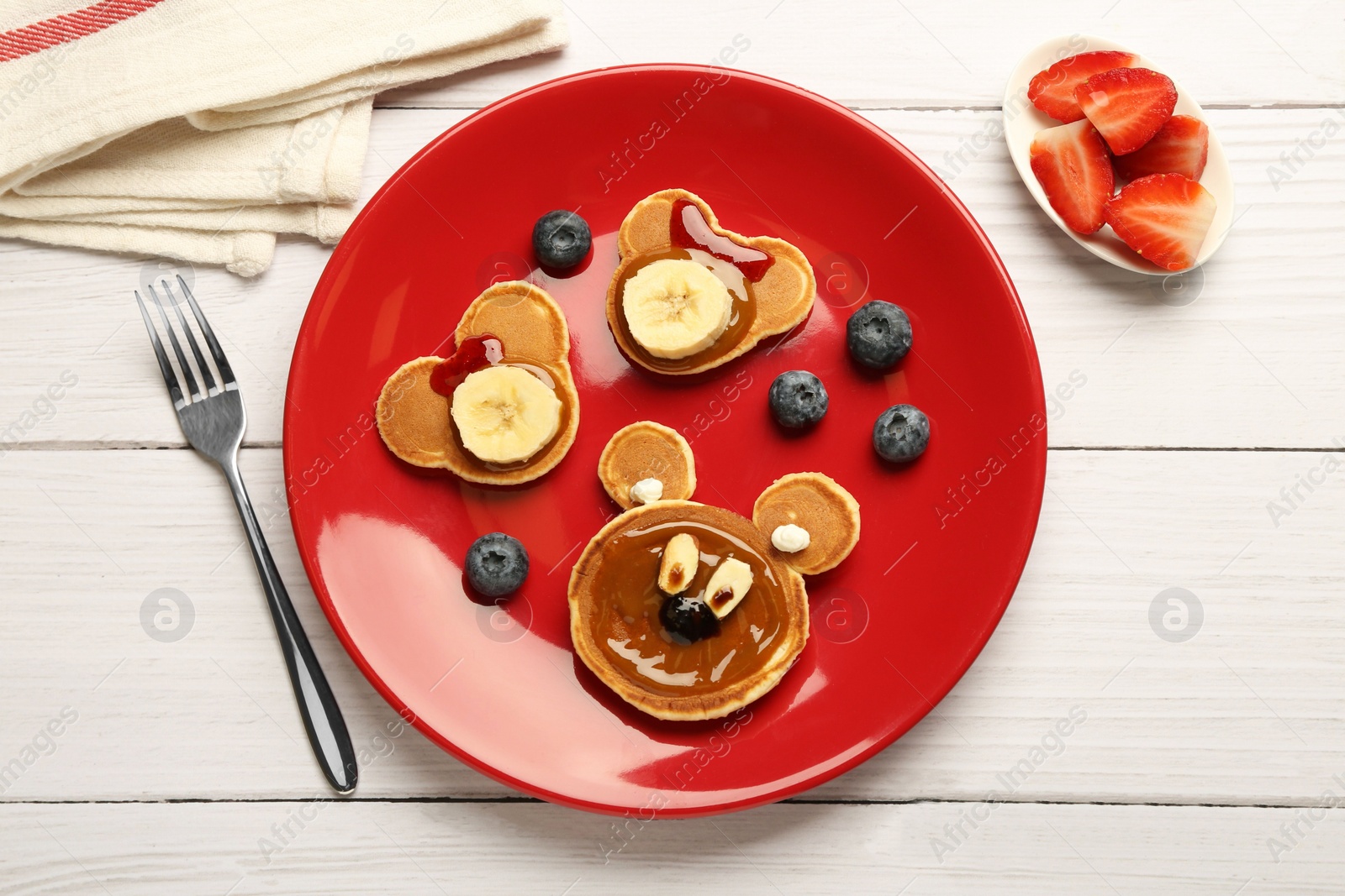 Photo of Creative serving for kids. Plate with cute bears made of pancakes, berries, banana and chocolate paste on white wooden table, flat lay