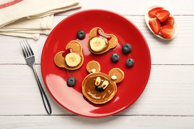 Creative serving for kids. Plate with cute bears made of pancakes, berries, banana and chocolate paste on white wooden table, flat lay