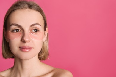 Photo of Beautiful young woman with under eye patches on pink background, space for text