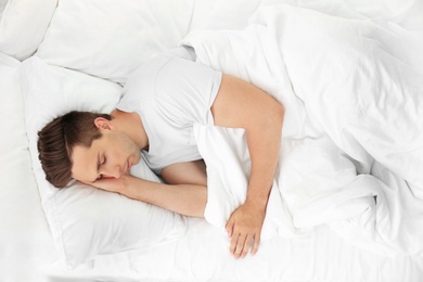 Photo of Young man sleeping on soft pillows in bed at home