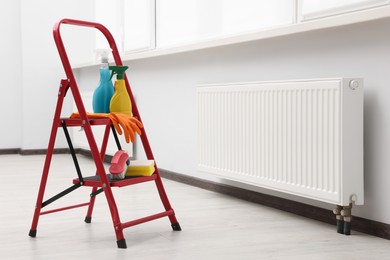 Photo of Ladder with cleaning supplies near modern radiator in room