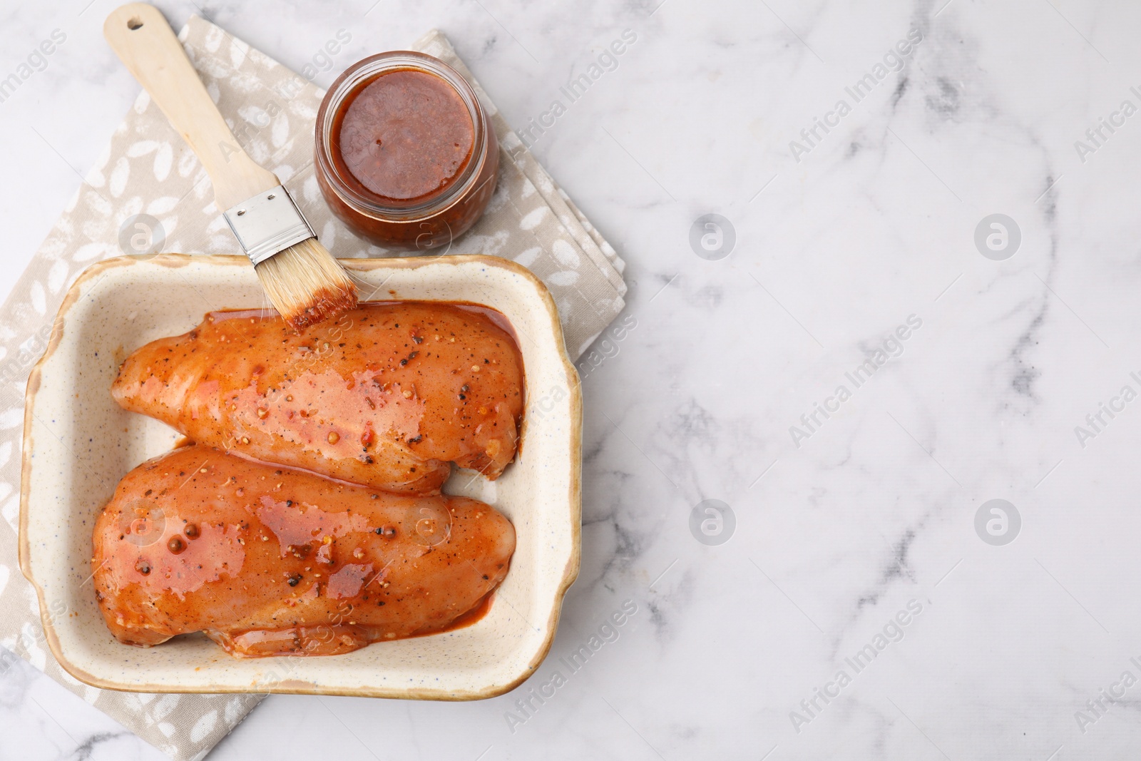 Photo of Raw marinated chicken fillets and basting brush on white marble table, flat lay. Space for text