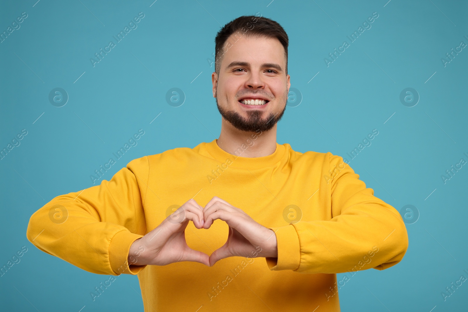 Photo of Man showing heart gesture with hands on light blue background