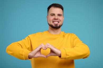 Man showing heart gesture with hands on light blue background