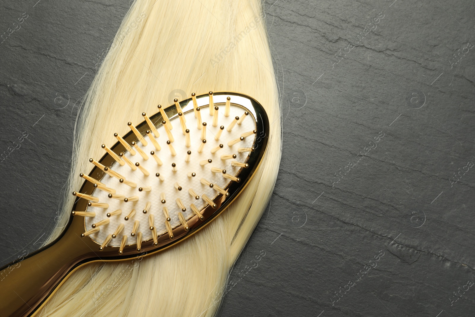 Photo of Stylish brush with blonde hair strand on dark grey table, top view. Space for text