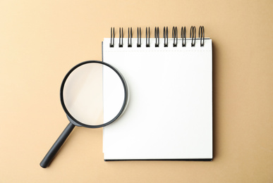 Photo of Magnifier glass and empty notebook on beige background, flat lay with space for text. Find keywords concept